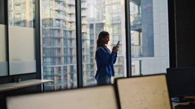 İş kadını, modern ofisteki cep telefonunu kullanarak online alışveriş yapıyor. Gülümseyen kadın yönetici iş yerindeki akıllı telefon uygulamasında internet siparişi veriyor. Mutlu bayan girişimci mesajları okuyor.