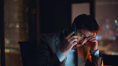 Yorgunluktan bitap düşmüş profesyonel gece ofis portresi. Stresli iş adamı telefonda konuşuyor. Kapalı kapılar ardında yorgun hissediyorum. Akıllı telefon konuşmalarında iş raporlarını çözmede çok çalışan mali muhasebeci sorunu