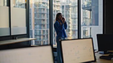 Gülümseyen kadın ofis müdürü pencerede telefonla konuşuyor. Modern akıllı telefon kullanarak müşterilerle konuşan çekici, zarif bir iş danışmanı. Mutlu bayan işçi telefonda danışmanlık yapıyor.