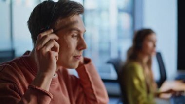 Operatör eli kulaklıkları bilgisayardan alıyor. Genç adam ofisteki çağrı merkezinde danışmanlık yapıyor. Pozitif destek ajanı kulaklıkla konuşuyor. Müşteri hizmetleri yardım hattı kavramı 