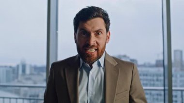 Büyük ofis pencerelerine bağıran öfkeli CEO portresi. Kızgın kızgın patron kameraya bakıyor ve duygusal olarak el kol hareketi yapıyor. Şık takım elbiseli stresli lider kasvetli şehir işyerinde gerginliğini dile getiriyor.