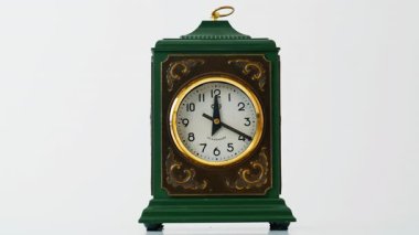 Enfes saat dairesel olarak kapalı mekanda zamanı gösteriyor. Eski metalik yeşil birliklerle beyaz arka planda duran zarif klasik bir cihaz. Pürüzsüz bir yüzeye yerleştirilmiş klasik ev dekoru. Eski tarz