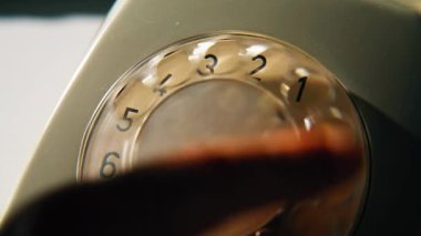 Evdeki sabit cihazda elle çevirmeli telefon. Kapalı alandaki klasik telefondan plakalı diski çeviren adam parmağı. Tanımlanamayan adam iletişim için retro dönüş mekanizmasına çağrı yapıyor.