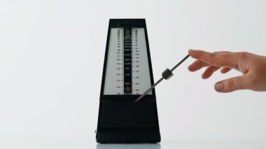 Müzisyen eli, beyaz masadaki metronomu ayarlıyor. Tempo aleti ritmik bir şekilde sallanarak kontrol hissi yaratıyor. Tanımlanamayan bir adam sarkaçı içeri itiyor. Müzik taktiği ölçüm kavramını yendi