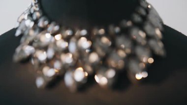 Moda mücevheri tasması nötr stüdyonun içinde parlıyor. Kesilmiş taşlar ışığı yansıtır. Siyah tekstil büstünün üzerinde duran parlak taş kolye. Büyük mücevherler.
