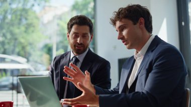 İki yönetici restoranda laptopu videoya çekiyor ve olumlu bir ifadeyle kapatıyorlar. Kafe masasında iş birliği yapan profesyonel iş arkadaşları. Kafeteryada çalışan iş arkadaşları bilgisayara bakıyor