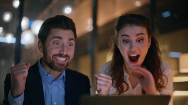 Başarılı ortaklar, gece ofisindeki dizüstü bilgisayarla anlaşmayı kazandılar. Duygusal iş arkadaşları akşam işyerlerinde iş zaferlerini kutluyorlar. Finansal gelir konusunda heyecanlı iş adamları.