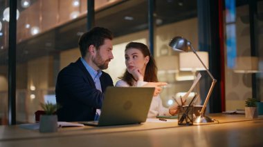 Yaratıcı girişimciler akşam geç saatlerde modern ofiste oturarak strateji tartışıyorlar. İki iş arkadaşı, karanlık işyerindeki gazete okuma projesinde işbirliği yapıyor. Uzlaşma üzerinde çalışan gülümseyen meslektaşlar.