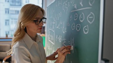 Üniversite karatahtasında matematik öğreten kadın öğretmen. Okulun kara tahtasında matematik denklemlerini çözen gözlüklü zeki bayan öğretmen. Profesyonel eğitim kavramı.