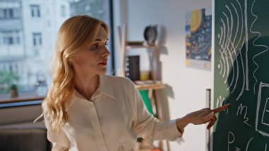 Üniversite profesörü formülleri karatahtaya yakın planda açıklıyor. Tahtaya matematik denklemleri yazan bayan eğitimci bilinmeyen öğrencilerle konuşuyor. Üniversitede matematik öğreten profesyonel bir kadın..