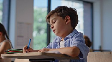 Sınıf arkadaşları yakın planda ders çalışıyor. Kitaplara yazı yazan ilkokul çocuklarına odaklanmış oturma masaları. Küçük okul çocukları sınıfta ders alıyor. İlköğretim.