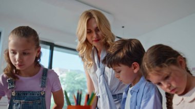Sanat sınıfında resim yapan ilkokul öğrencileri. Dost canlısı bayan öğretmenler grup öğrencilerini sınıfta yaratıcılıkla meşgul ediyor. Çocuklar boya kullanarak renkli resimler yapıyorlar. Yaratıcı etkinlik