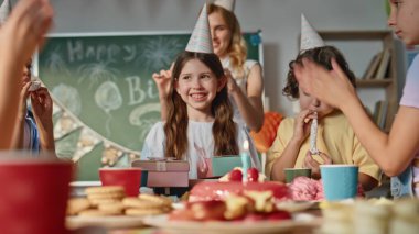Arkadaşları sürpriz bir doğum günü kutlaması yapıyor. Şenlikli bir sınıfın yakın çekiminde. Mutlu okul çocukları gülümseyen liseli kızı kutluyor. Neşeli kadın öğretmen olayın videosunu çekiyor.