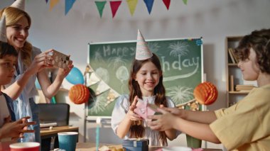 Süslü sınıfta neşeli doğum günü kutlamalarında gülümseyen liseli kız hediyeler alıyor. Neşeli anları paylaşan arkadaşlarla çevrili mutlu bir kız. Neşeli okul çocukları sınıfta eğleniyor.
