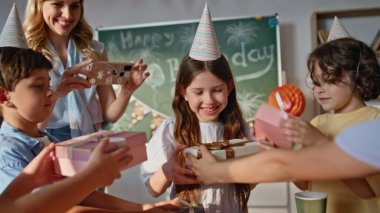 Çocuklar doğum günü kızını kutluyorlar hediye kutularını kapatıyorlar. Neşeli sınıf arkadaşlarıyla el çırpan mutlu liseli kızlar. Gülümseyen kadın öğretmen telefonda festival etkinliğini kaydediyor..