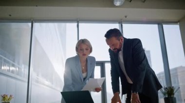 Ofis yöneticileri iş yerinin düşük açılı görüntüsüne bakıyor. Gülümseyen iş kadını birlikte çalışan iş arkadaşına evraklarını gösteriyor. Olumlu erkek kadın işçiler proje sonuçlarından memnun.