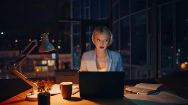 Yaratıcı yönetici video çağrısı proje fikrini karanlık ofis kapanışında açıklıyor. Geceleri dizüstü bilgisayarla konuşan gülümseyen bir kadın. Pozitif sarışının uzak kabinede online iş görüşmesi var.