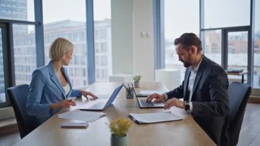 Ofis muhasebecileri modern yüksek katlı çalışma alanındaki belgeleri inceliyor. Şirket planlama tartışmalarıyla meşgul iş arkadaşları evrak işleriyle uğraşıyorlar. İki ortak dizüstü bilgisayar masasında sözleşmelerle oturuyor.