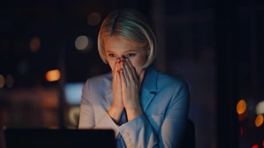 Neşeli kazanan, gece ofisindeki kapanış videosuyla duygularını gösteriyor. Heyecanlı iş kadını tepki göstererek karanlık işyerindeki sanal toplantıyı kazanıyor. Duygusal kadın patron dizüstü bilgisayarlı webcam ile seviniyor. 