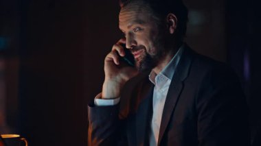 Geç saatte çalışan işçilerin karanlık dolaptan cep telefonlarını aradığı portre. Kapalı çekimde gülümseyen CEO, gece ofisinde akıllı telefon kullanarak yabancı bir ortakla konuşuyor. İş adamının cep telefonu görüşmesi var. 