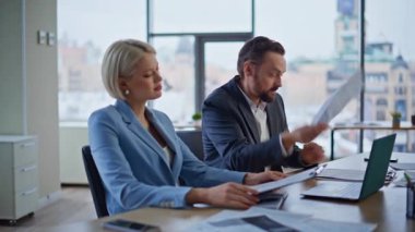 İş ortakları, kötü mali raporları yakın çekimde tutarken görüntülü görüşme ile tartışıyor. Öfkeli kadın, internetteki toplantı hakkında endişelenen belgeleri fırlatıyor. Öfkeli iş arkadaşları web kamerası kapağını kapatsın diye bağırıyor.