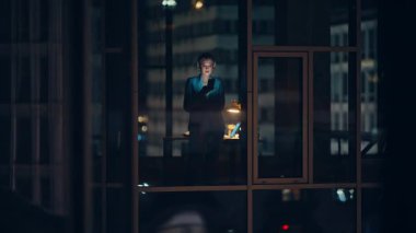 Siluetli iş kadını ofis penceresinde duruyor ve gece lambası ışığında tek başına akıllı telefon yazıyor. Bilinmeyen bir bayan direktör iş yerinde geç saatlere kadar kalan cep telefonuyla mesajlaşıyor. Kurumsal yalnızlık