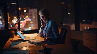 Profesyonel danışman, akşam şirketinin çalışma alanından müşteriyi arıyor. Meşgul kadın yönetici cep telefonuyla konuşuyor. Gece ofisinde dizüstü çalışıyor. Gülümseyen iş kadını cep telefonu konuşmalarıyla projeyi tartışıyor