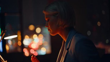 Geç kalmış bir iş kadınının karanlık çalışma alanında kapalı oturmaktan bitkin düşmesi. Yorgun ofis çalışanı fazla mesai yapmadan kafasına dokunuyor. Yorgun sarışın iş gününde baş ağrısı çekiyor.