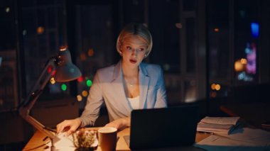 Sanal konferansta konuşan başarılı bir çalışan karanlık şirket ofisinde oturuyor. Gülümseyen iş kadını gece bilgisayarındaki video görüşmesinde belgeler gösteriyor. Çevrimiçi toplantıda pozitif sarışın sunum projesi