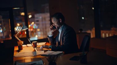Akşam şirketinin çalışma alanında profesyonel çalışan akıllı telefon görüşmesi. Meşgul bir yönetici, cep telefonunda müşteriyle konuşuyor. Gece ofisinde dizüstü çalışıyor. Gülümseyen işadamı cep telefonuyla projeyi tartışıyor