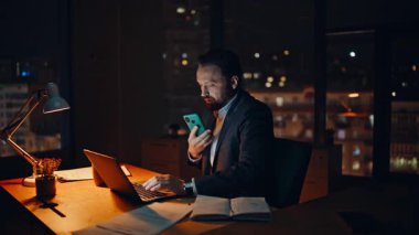 Bilgisayarda klavye yazan birden fazla görev yöneticisi karanlık ofiste oturuyor. Ciddi bir adam cep telefonuyla danışmanlık yapıyor. Bilgisayarda bilgi arıyor. Gece işçisi akıllı telefondan konuşuyor. Fazla mesai yapıyor.