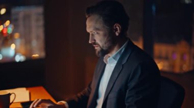 Geç yöneticimiz akşam ofiste dizüstü bilgisayarı elden ele kontrol ediyor. Öfkeli iş adamı, iş yerindeki hatalar yüzünden gergin ve sinirli bir şekilde bilgisayarın kapağını kapatıyor. Stresli patron şehir manzaralı işyerinde başarısız oldu