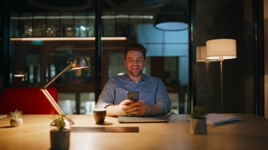 Lamba ışığı ofisinin altında cep telefonundan SMS okuyan geç çalışan bir işçi. Cep telefonuyla gece işyerinde sosyal medya içeriğini izleyen gülümseyen girişimci. Mutlu iş adamı gece vakti akıllı telefona bakar.