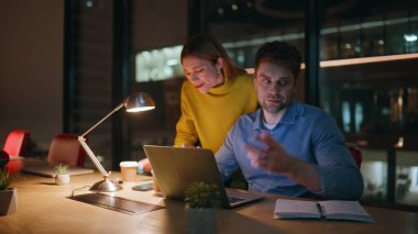İş meselelerini çözmek için fazla mesai yapan iki meslektaşım. Stresli yönetici dizüstü bilgisayarı kapatırken proje başarısız oldu. İş kadını, karanlık şirket işyerindeki iş arkadaşını rahatlatıyor..
