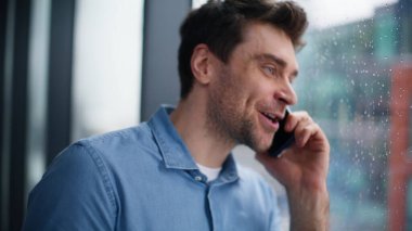 Gülümseyen işadamı, yağmurlu şehir manzarasının penceresinden aramayı bitirdi. Mutlu adam akıllı telefon sohbetinin tadını çıkarıyor. Başarılı girişimci cep telefonunda iyi haberler duyuyor.