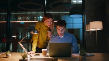 Aşırı mutlu iş arkadaşları, karanlık işyerinde beş sevinçli iş başarısı sağlıyor. Ofis bilgisayarında kahve fincanı arayan iki işçi heyecanlı. Duygusal kazananlar gece iş yerinde harika haberlere tepki veriyorlar.