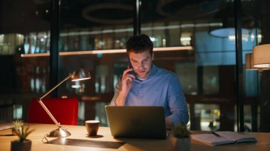 Şirketin profesyonel konuşan cep telefonu gece ofisinde yakın plan çekimde. Gülümseyen yönetici, karanlık işyerinde oturarak akıllı telefon görüşmesine danışmanlık yapıyor. Akıllı serbest çalışan cep telefonuyla fazla mesai yapıyor..