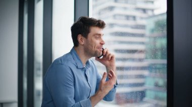 Panoramik pencerede bekleyen harika haberleri paylaşan çalışanları arıyorum. Duygusal iş adamı akıllı telefondan konuşuyor ve başarıyı tartışıyor. Yağmurlu şehir görünümlü cep telefonuyla konuşan yakışıklı yönetici.