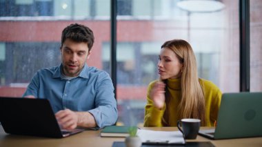 Ekip üyeleri açık alanda dizüstü bilgisayar ekranı projesini tartışıyor. Gülümseyen kadın, erkeğe iş birliği teklif ediyor. Bilgisayarlarda çalışan iki meslektaşım panoramik pencerede oturuyor..