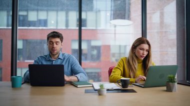 Şirket çalışma alanına dizüstü bilgisayar arayan motivasyonsuz iş arkadaşları. Yorgun erkek kadın ofis panoramik penceresinin yanında aşırı yüklü iş projesi. İki yönetici birlikte çalışırken yorulduklarını hissediyorlar..