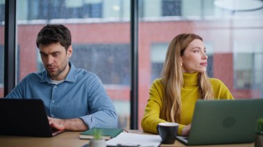 Çevrimiçi çalışan iki serbest çalışan panoramik ofis penceresinin önünde oturuyorlar. İki iş arkadaşı pazarlama araştırması yapan dizüstü bilgisayarlara odaklanmış. Ortak çalışma alanında bilgisayar yazan kendine güvenen şirket yöneticileri