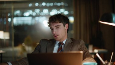 Çok çalışan yaratıcı, karanlık ofiste dizüstü bilgisayarlı masa başında çalışan kağıtlara bakıyor. Kapalı alanda çalışan bitkin yönetici