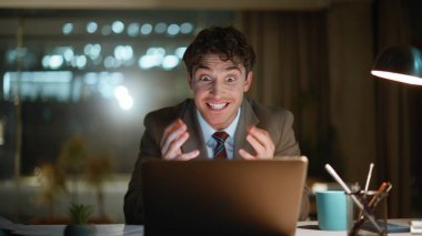 Gece kazananı dizüstü bilgisayarla ofisteki yakın çekimlerde iyi haberlerin tadını çıkarıyor. Aşırı neşeli iş adamı karanlık işyerinde e-posta okuyarak neşeli işler yapıyor.