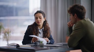 Ofis akıl hocası stajyerliği öğreniyor. Elinde kağıtlarla masa başında oturuyor. Kendine güvenen iş kadını iş toplantısında adamla belgeleri tartışıyor.