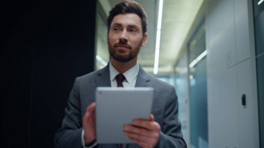 Neşeli lider modern ofis koridorunda tablet yürüyüşü yapıyor. Mutlu CEO uzmanı başarılı sonuçları kontrol ediyor online e-postalar cam kapı girişine gidiyor. Zarif iş adamı meslektaşlarını selamlıyor