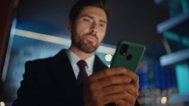 Gece lambaları caddesinde cep telefonuyla yazı yazan adam. Adam dışarıda akıllı telefondan mesaj yolluyor. Düşünceli CEO, karanlık şehir arka planında cep telefonu tutarak ekranlara dokunuyor.