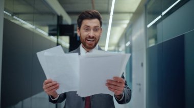 Kapanış uzmanı evrakları inceliyor. Ofis koridorunda heyecanlı hissediyorum. Duygusal iş adamı belgeleri fırlatıyor ve iş başarısını kutluyor. Koridorda el kol hareketi yapan çok mutlu bir acemi.