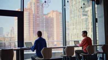 Panoramik pencerenin yanında aynı iş yerinde çalışan birkaç kişi. Modern çalışma alanında laptopları karıştıran iki serbest çalışan. İş akışı sırasında birbirleriyle konuşan pozitif meslektaşlar.