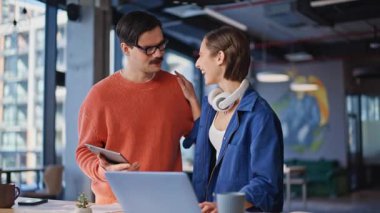 Şirket çalışanları, modern ofis alanında duran tablet verilerini tartışıyor. İki gülümseyen meslektaş iş yerinde harika haberler paylaşıyor. Profesyonel analistler iş belgelerini birlikte inceliyorlar..