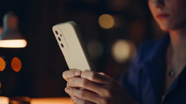 Karanlık çalışma alanında akıllı telefondan mesaj gönderen eller. Lamba ışığı ofisinde cep telefonuna mesaj atan tanınmayan bir iş kadını. Genç bayan girişimci cep telefonuyla online sipariş veriyor..